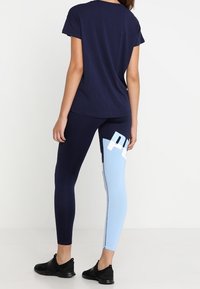 Námořnické tričko v kombinaci s legínami, které mají námořnické a světle modré části, velké bílé logování a hladký, elastický materiál.