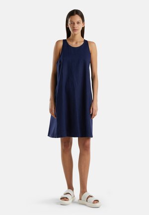 Vestido sin mangas azul marino de corte relajado, confeccionado en tela ligera, con cuello redondo y que cae por encima de la rodilla. Sandalias blancas de dedo.