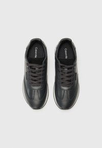 Zwarte sportschoenen met een glad leren bovenkant en gestructureerde details. Voorzien van ronde veters en een witte rubberen zool. Merklogo zichtbaar aan de binnenkant.