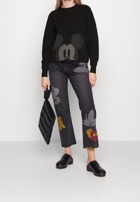 Czarny sweter z okrągłym dekoltem z dużą szaro-skalową grafiką Myszki Mickey. Ciemnoszare, krótkie jeansy z kolorowymi wzorami z bajek. Czarne klapki z ćwiekami.