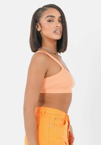 Perzikkleurige geribde crop top met brede banden, gecombineerd met feloranje high-waisted jeans. Glad textuur en strakke pasvorm.
