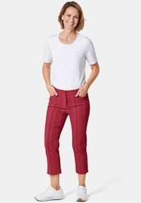 Weißes kurzärmeliges Hemd, rot gemusterte, knöchellange Hose und weiße Turnschuhe. Die Hose hat vertikale Streifen und einen vorderen Knopf.