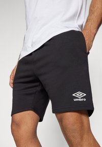 Bermudas de algodón negras con un diseño ajustado, que presentan un logo blanco de Umbro en el muslo y sin patrones visibles ni detalles de hardware.