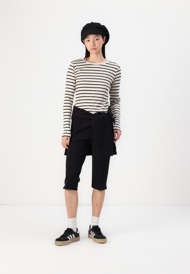 Haut à rayures à manches longues en crème et noir, associé à un short noir à mi-cuisse. Porté avec un béret noir et des baskets noires avec des rayures blanches.