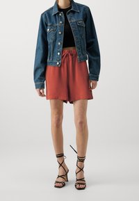 Farkkutakki napilla, musta crop top, ruosteenväriset sortsit naruilla, ja mustat nauhaliuskat. Sulavat tekstuurit ja rento tyyli.