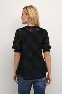 Črna čipkasta majica z rožnatim vzorcem, kratkimi puff rokavi in valovitimi robovi. V kombinaciji z modrimi kavbojkami, ki prikazujejo ohlapno prileganje.