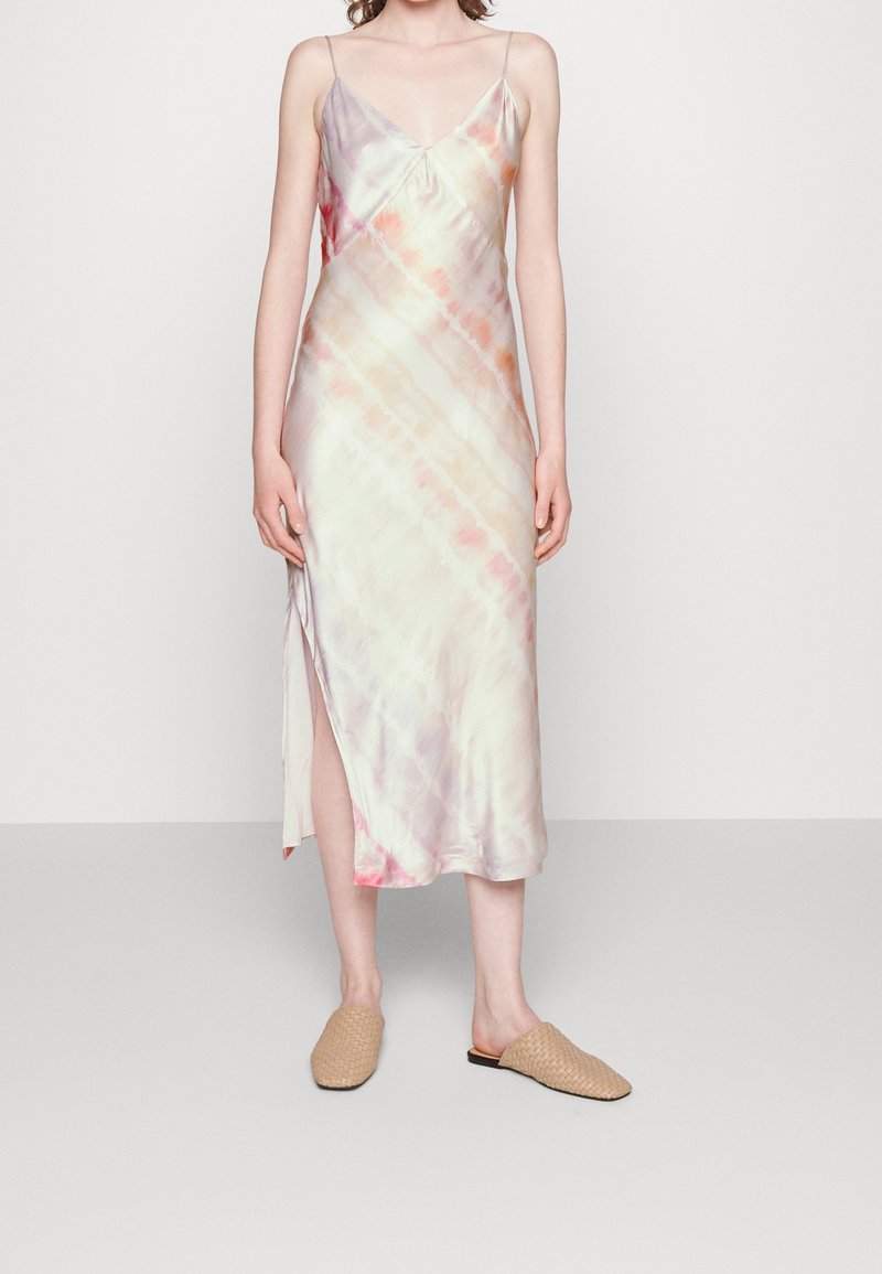Robe midi sans manches ajustée avec motif tie-dye pastel, fente latérale et chaussures beiges tissées à enfiler sur une personne debout.