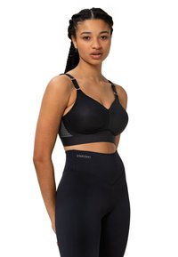 Schwarzer Netz-Sport-BH mit verstellbaren Trägern, ausgestattet mit einem glatten Unterband und geometrischem Muster an der Seite. Kombiniert mit hochtaillierten schwarzen Leggings.