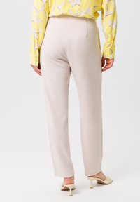 Lichtbeige broek met een rechte pasvorm, een gladde textuur en subtiele naaddetails, gecombineerd met pale, hoge mules.
