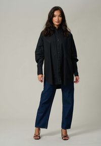 Sort oversized skjorte med knaplukning og lange ærmer, parret med løse mørkeblå jeans og sorte strop hæle sandaler.