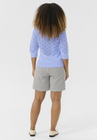 Svetlo modra pletena jopica s vzorjem na hrbtu in srokavčki do tri četrtine, v kombinaciji s kratkimi hlačami črno-bele proge.