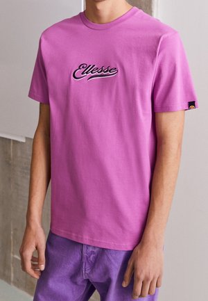 T-shirt en coton rose avec un col rond et des manches courtes, arborant le logo "Ellesse" brodé en noir et blanc sur la poitrine.