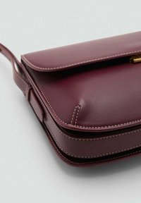 Borsa a tracolla in pelle bordeaux con chiusura a patta, cuciture superiori e design piatto e strutturato. Presenta una tracolla sottile e hardware in tono oro.