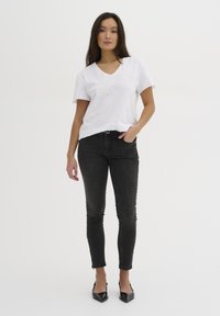 Camiseta de algodón blanca con escote en V y mangas cortas, combinada con jeans skinny de mezclilla oscura que tienen un detalle de cremallera en los tobillos, y tacones negros de punta.