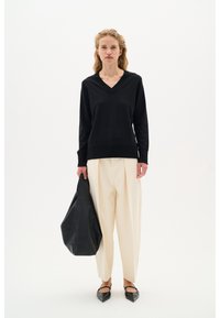 Maglione nero a scollatura a V con orlo a coste, pantaloni larghi crema e borsa nera in pelle. Le ballerine nere a punta completano l'outfit neutro.