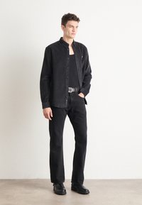 Camisa de mezclilla negra con botones sobre una camiseta negra ajustada, combinada con jeans negros de pierna recta y botas negras de suela gruesa. Diseño simple.