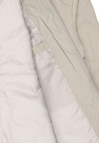 Interno di giacca trapuntata grigio chiaro con un rivestimento beige liscio. Presenta una cerniera e una tasca nascosta sul lato sinistro. Tessuto testurizzato.