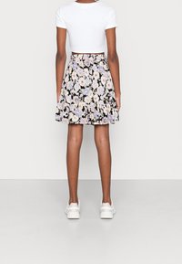 Kukkamekko mustalla taustalla, jossa on purppuran- ja valkoinen kukkakuosi. Valmistettu kevyestä kankaasta, jossa on levenevä helma ja leikkisä rypytys.