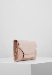 Růžové psaníčko se semišovou klopou, zlatými kovovými doplňky a řetízkovým popruhem. Hladká textura a obdélníkový tvar s nakloněnými okraji.