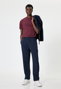 T-shirt bordeaux e pantaloni blu scuro, abbinati a un blazer scuro. Il modello indossa sneaker bianche. Il tessuto è liscio; il design è casual ma curato.