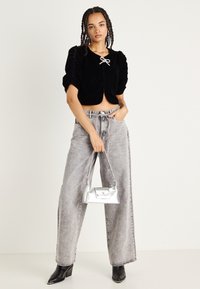 Top in velluto nero cropped con maniche a sbuffo e dettaglio a fiocco, abbinato a jeans grigi a vita alta e gamba larga, e una borsa argento.