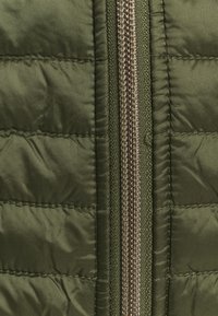 Oliwkowa kurtka puchowa z tkaniny o pikowanej strukturze i metalowym zamkiem błyskawicznym, charakteryzująca się gładkim wykończeniem i pionowymi przeszyciami.