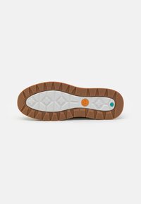 Gummiyttersula med ett mönstrat mönster i brunt och vitt. Har en cirkulär orange logotyp och en liten grön accent. Robust och strukturerad design.