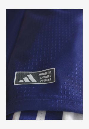 Tela azul con una textura suave que presenta una etiqueta en blanco y negro con el texto "PRODUCTO LICENCIADO AUTÉNTICO" junto al logo de Adidas.