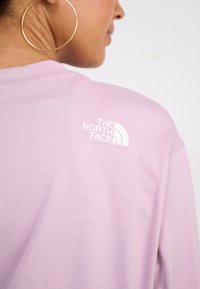Hellblaues T-Shirt aus weichem Material, mit einem weißen gestickten Logo von 'The North Face' im Bereich der hinteren Schulter.