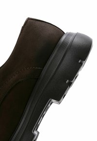 Bottine en cuir marron avec un dessus texturé, dotée d'une semelle en caoutchouc noir avec un design nervuré et un détail sur le côté.