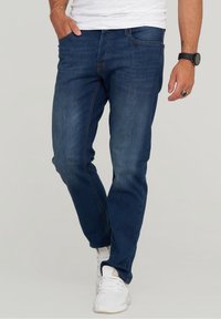 Blå denimjeans med slim fit, med orange sömmar, klassisk femficksdesign och sliten textur, tillsammans med vita sneakers.