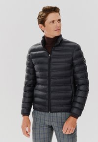 Czarna kurtka puchowa z pikowanym wzorem, wysokim kołnierzem i zapięciem na zamek. Miękka, błyszcząca tekstura; zawiera logo na lewym rękawie.