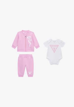 Pinkfarbige Jacke mit Reißverschluss und Hose mit weißem "GUESS"-Schriftzug, kombiniert mit weißem Kurzarm-Body mit pinkem "GUESS"-Logo auf der Vorderseite.