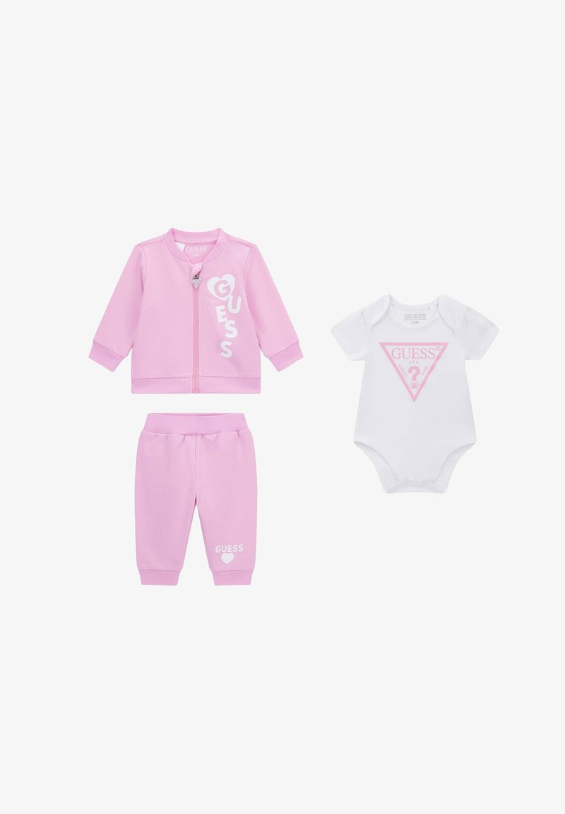 Różowa bluza zapinana na zamek i spodnie z białym napisem „GUESS”, zestawione z białym body z krótkim rękawem, z różowym logo „GUESS” z przodu.