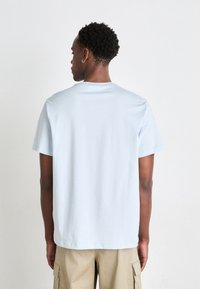 Camiseta de algodón azul claro con mangas cortas, escote redondo y corte relajado, vista desde la parte de atrás. Sin patrones o acentos visibles.