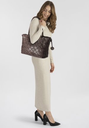 Sac en cuir marron avec un motif de diamants matelassé, doté de doubles poignées et d'un charme décoratif, complété par une robe crème douce.