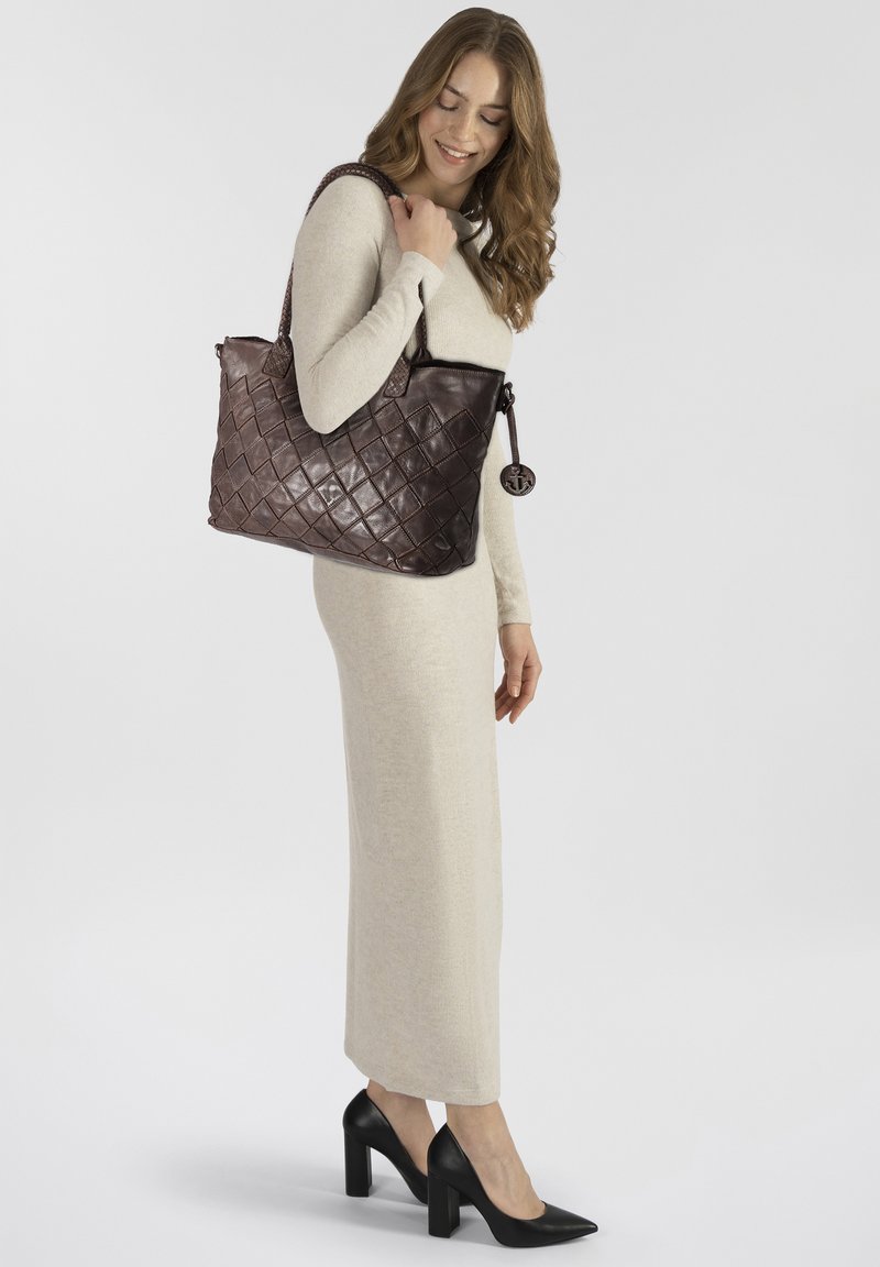 Sac en cuir marron avec un motif de diamants matelassé, doté de doubles poignées et d'un charme décoratif, complété par une robe crème douce.