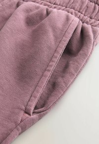 Lilla bomuldsjoggers med en tekstureret stof, der har en elastisk talje og sidelommer for funktionalitet.