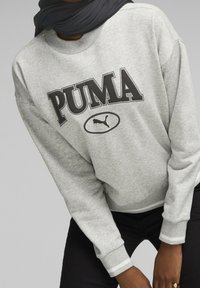 Felpa grigio chiaro con logo "PUMA" in nero. Polsini e bordo in costina con righe bianche. Tessuto morbido e strutturato. Vestibilità casual.