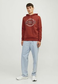 Bordeaux hættejakke med hvid grafik tekst, parret med lyseblå baggy jeans og hvide sneakers. Hættejakken har snoretræk og ribbede manchetter.