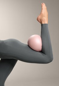 Top attivo grigio aderente con righe testurizzate. Un oggetto semisferico rosa e liscio poggia sul gomito, migliorando la posizione del braccio.