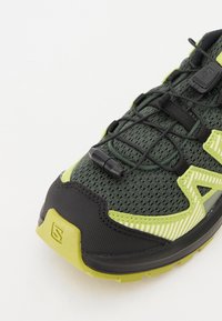 Zelená a černá sportovní bota s mesh svrškem, rychlým zavazováním a strukturovanou gumovou podrážkou; obsahuje reflexní pruhy a detaily.