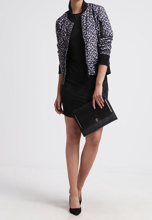 Veste bomber à imprimé léopard noir et blanc, robe cintrée noire et pochette noire avec des accents en métal doré. Portés avec des talons noirs.