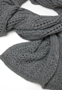 Écharpe tricotée en gris avec un motif texturé, mettant en avant des points torsadés et des fils métalliques subtils tissés tout au long. Apparence douce et chaude.