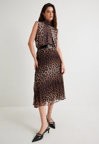 Vestito con stampa leopardata, colletto alto, gonna plissettata e cintura nera. Indossato con décolleté nere con tacco a rocchetto, caratterizzate da punta affusolata.