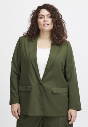 Olivově zelený blazer s výstřihovými klopami, dvěma předními kapsami a zapínáním na jeden knoflík. Nositelný přes bílý top bez rukávů, hladká textura látky.