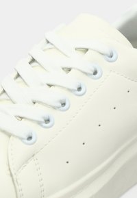 Sneaker in pelle bianca con lacci bianchi piatti, occhielli azzurri chiari, sottili perforazioni laterali e una texture liscia.