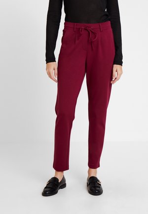 Woman wearing burgundy high-waist tapered pants with a drawstring and black loafers, standing against a plain white background.