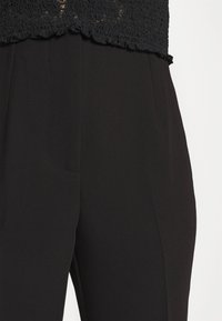 Black trousers featuring a smooth texture, tailored design, and discreet front pocket. Hem and fabric appear crisp and structured.