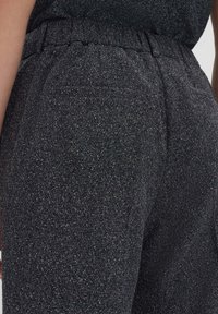 Pantalons gris foncé en tissu texturé avec un motif subtile de points, dotés d'une taille élastique et de poches latérales.